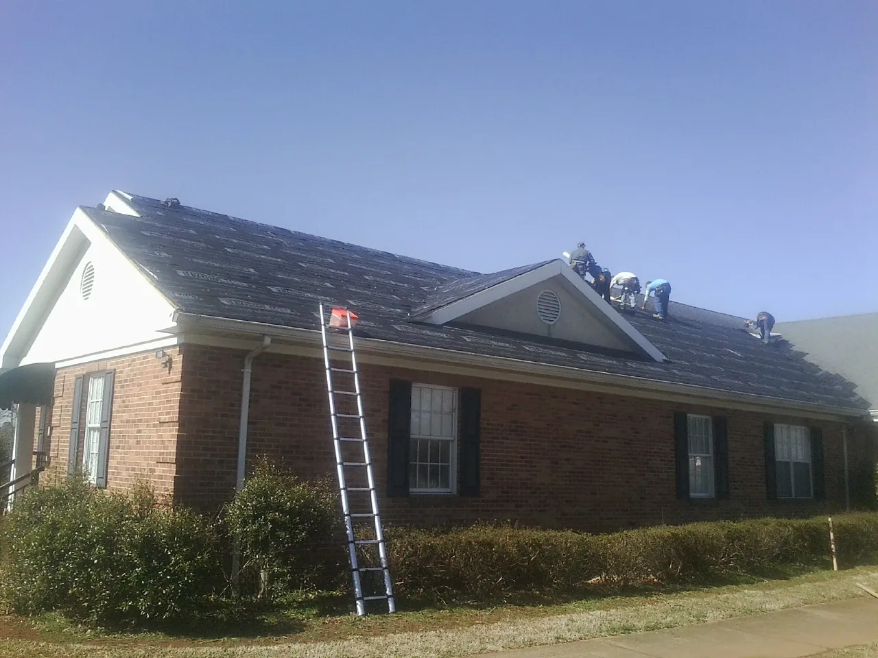 Crew tearing shingles off a brick ranch roof with a ladder set — Metal Roof Repair work by our crew in Westover