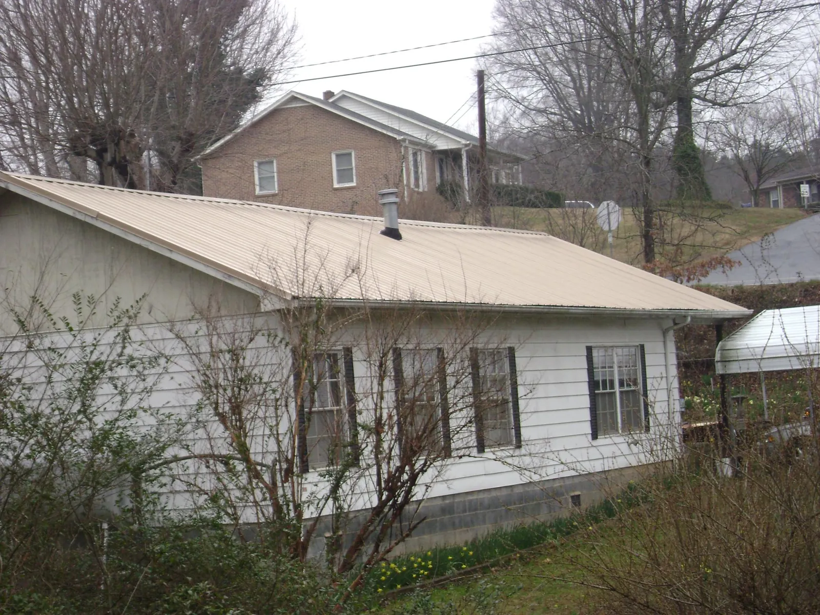 Tan metal roof on a white sided house set into a hillside — Commercial Roofing by Roofing Brothers in Westover